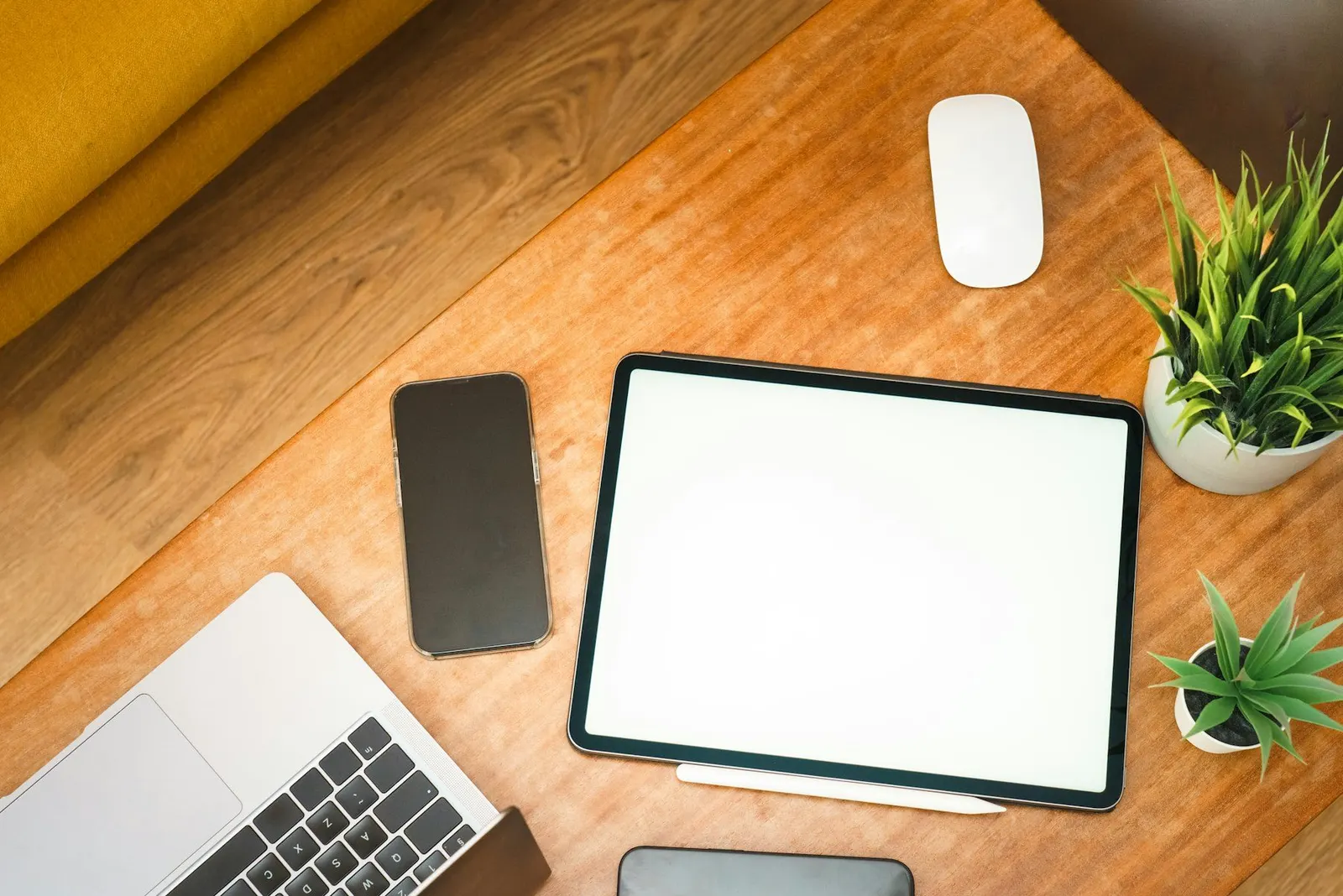 Bureau en bois vu du dessus avec une tablette, un smartphone, un ordinateur portable et une souris