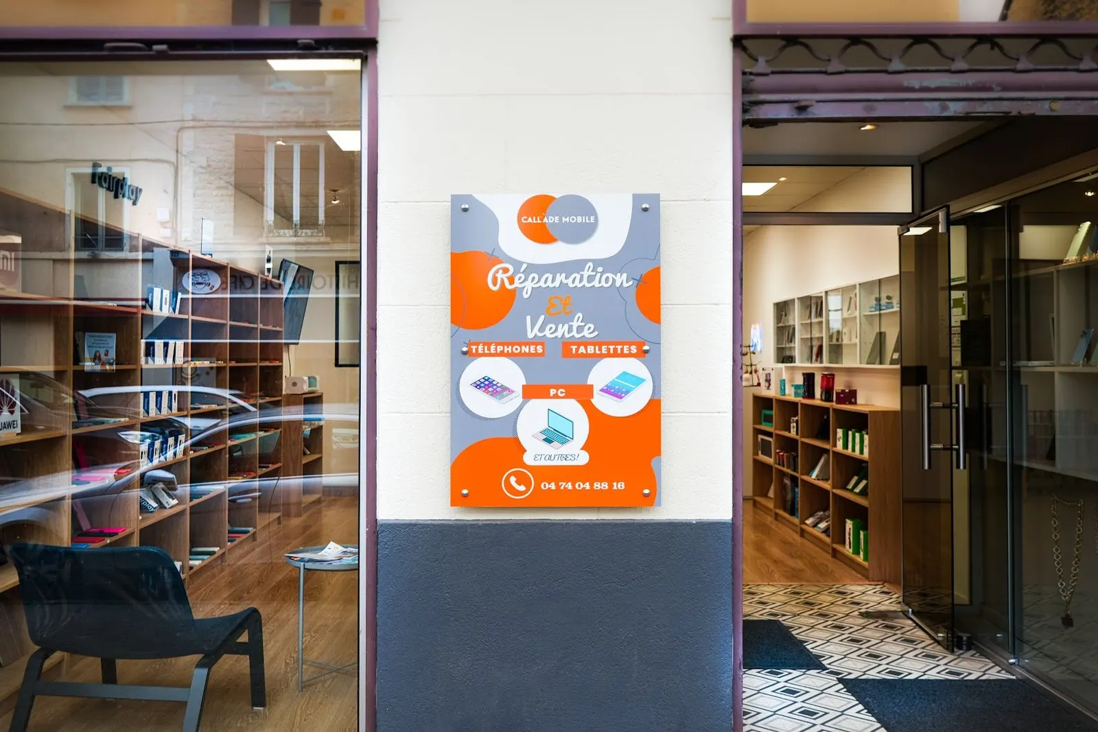 Entrée de la boutique de Belleville : panneau orange Réparation et Vente avec le numéro 04 74 04 88 16, vitrine et porte vitrée
