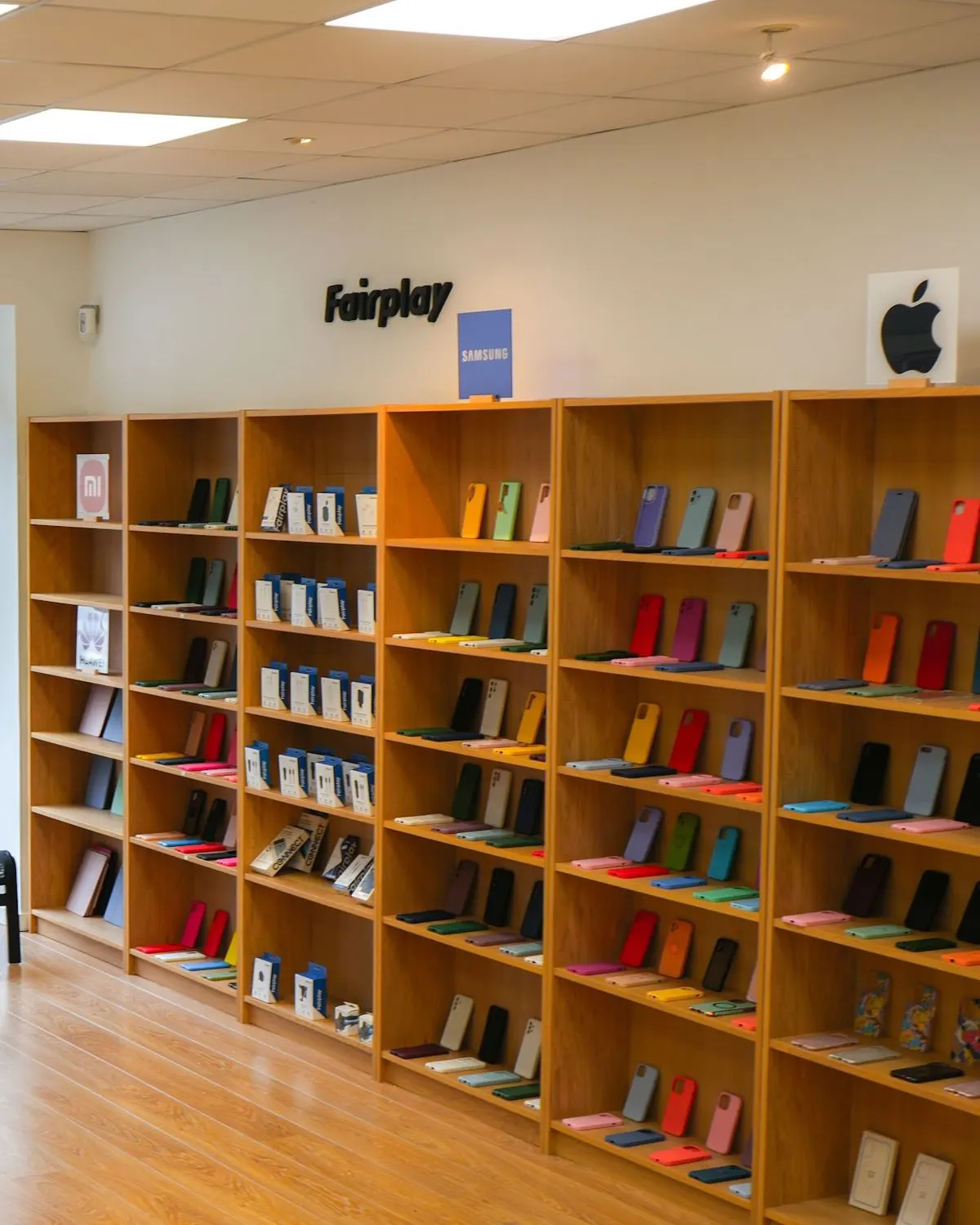 Intérieur de la boutique de Belleville-en-Beaujolais : étagères de bois clair remplies de coques de couleur, logos Samsung et Apple au mur
