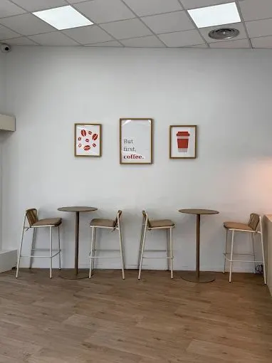 Coin d'attente de la boutique : quatre tabourets de bois, deux tables hautes, trois cadres au mur blanc