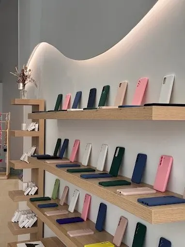Étagères de chêne clair sous le mur en vague éclairé, coques de téléphone rangées par couleur