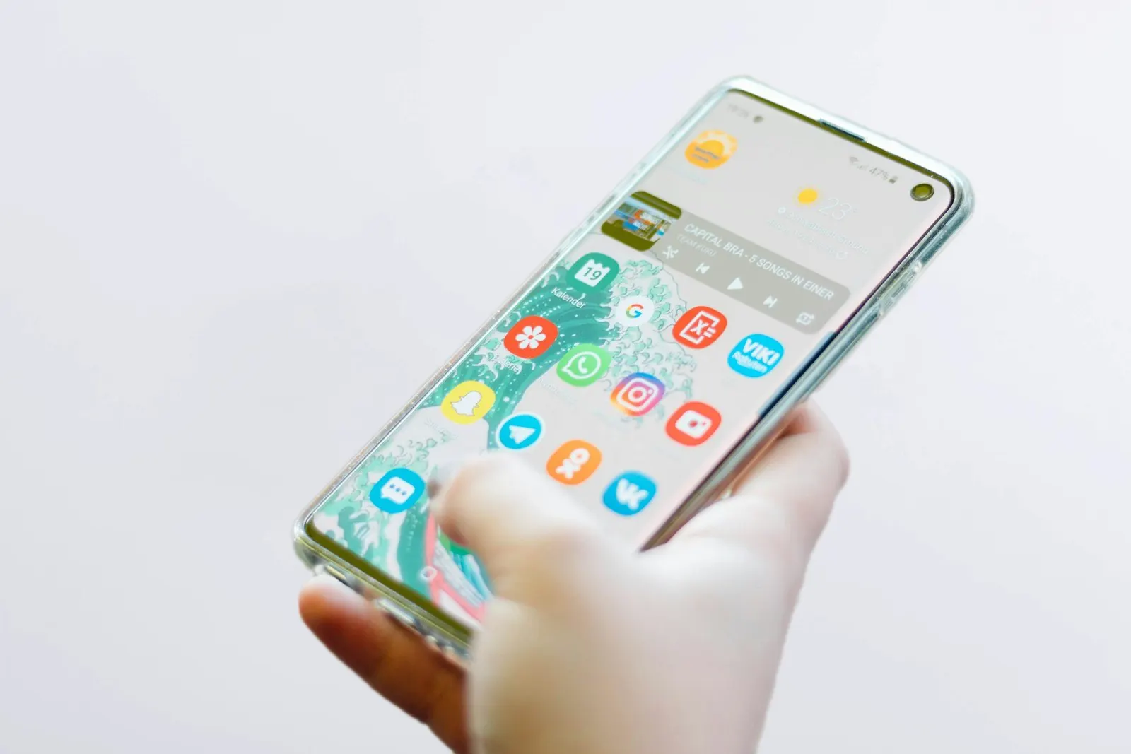 Main tenant un smartphone dont l'écran d'accueil affiche une grille d'applications, sur fond blanc