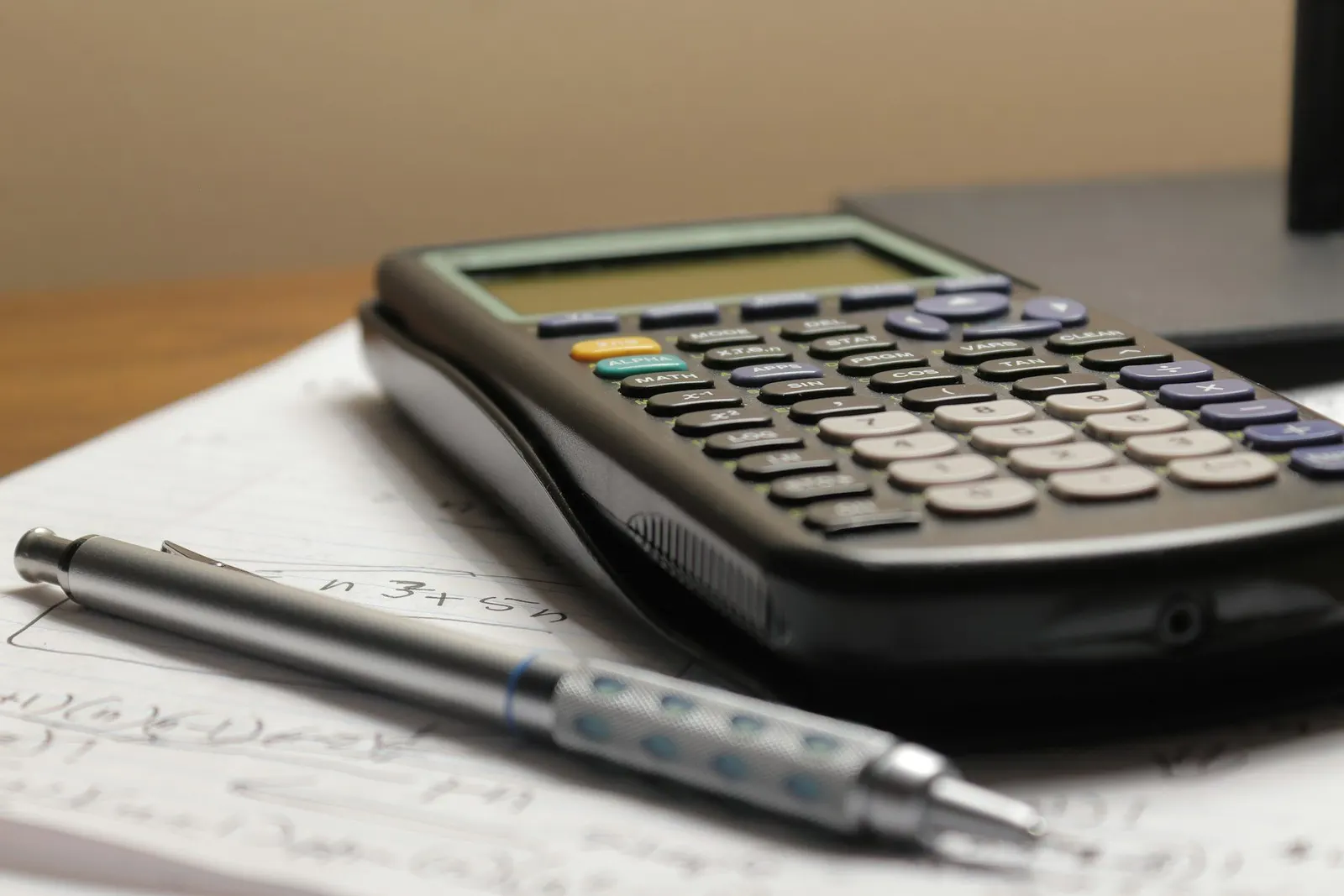 Calculatrice et porte-mine posés sur une feuille de calculs manuscrits